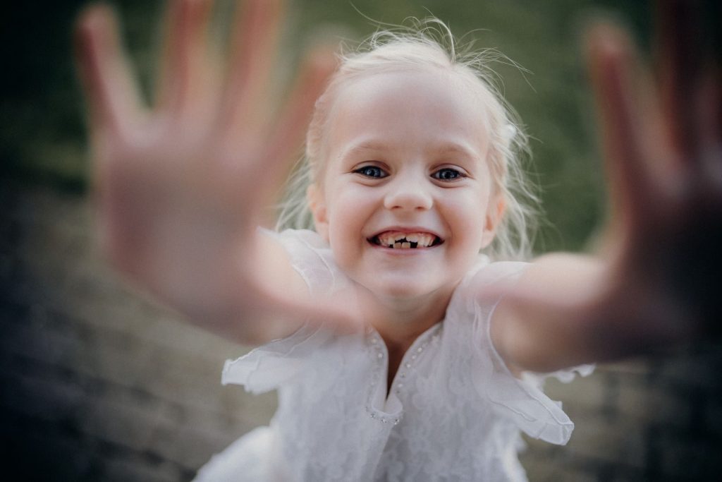 A happy blonde girl smiling widely, reaching out with joy and innocence.