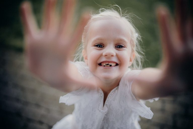 A happy blonde girl smiling widely, reaching out with joy and innocence.
