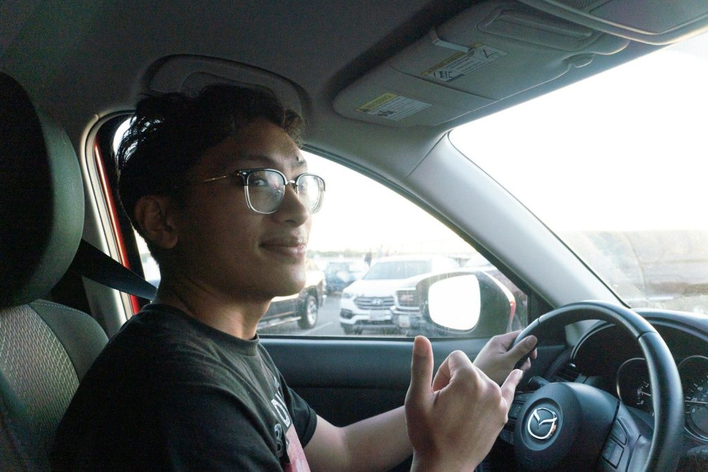 Young man driving a car and making a shaka gesture