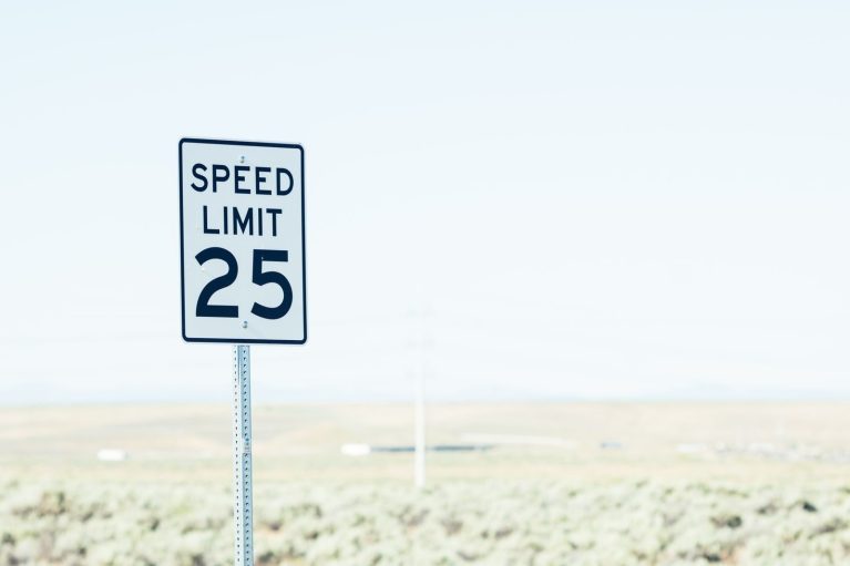 White sign on roadside with speed limit against empty green field at daytime