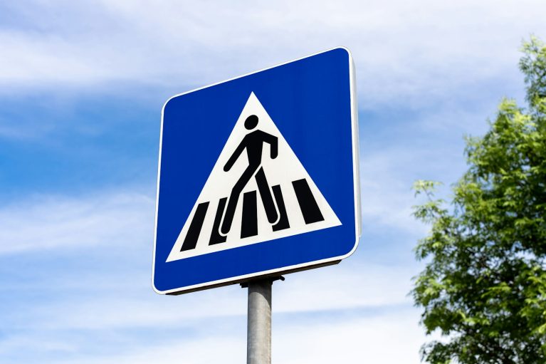 a blue and white pedestrian crossing sign with trees in the background