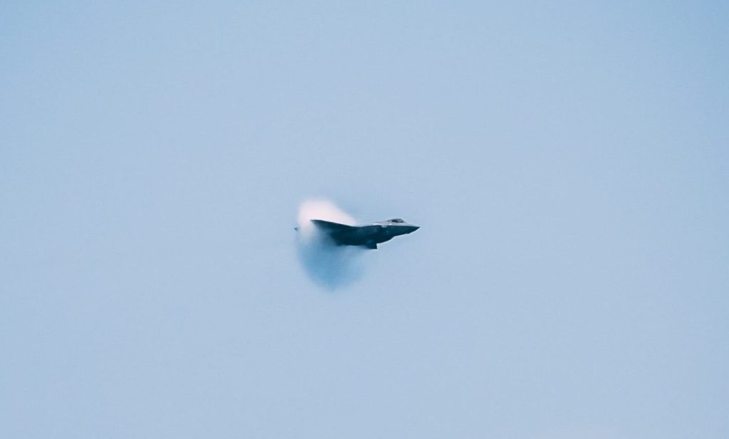 jet fighter creating sonic boom over the sea with ships