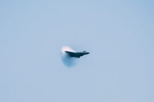 jet fighter creating sonic boom over the sea with ships