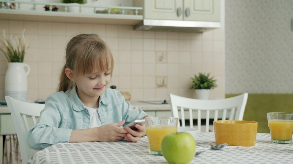 Girl using smartphone at kitchen table with breakfast