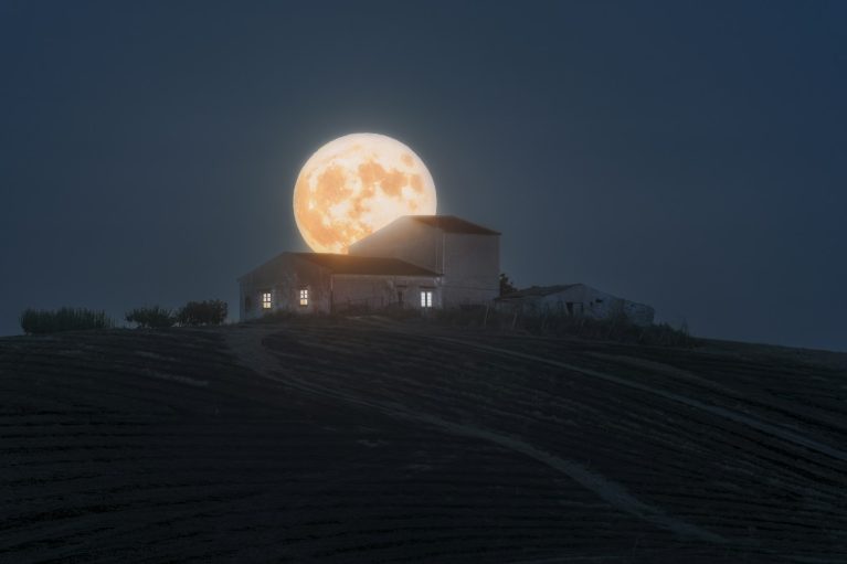 Full moon rising behind a house at night
