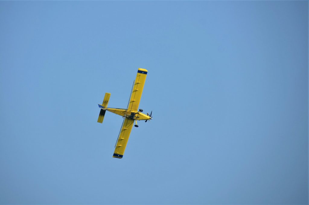 a small yellow airplane flying through a blue sky