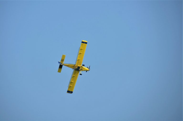 a small yellow airplane flying through a blue sky
